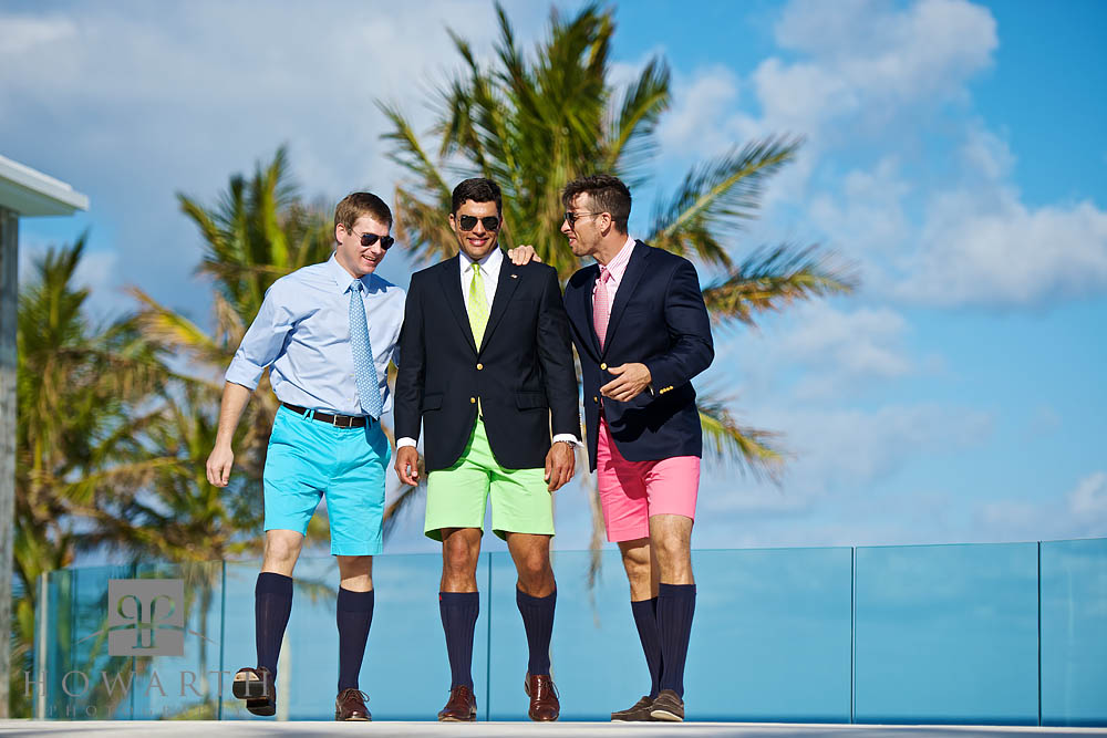 Three young professionals having a conversation wearing brightly colored blue, green and pink Bermuda Shorts, ties, jackets and...