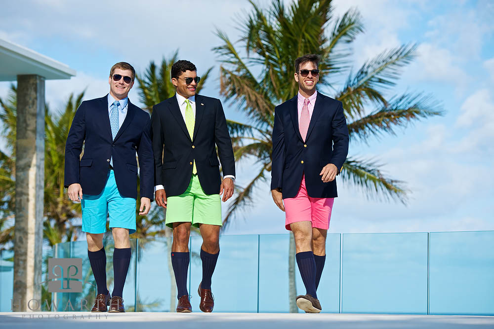 Three young professionals walking together; smiling and laughing while wearing brightly colored blue, green and pink Bermuda...