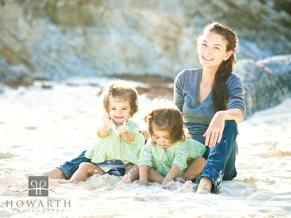 Mother sitting on the beach with her two young twin daughters playing in the sand