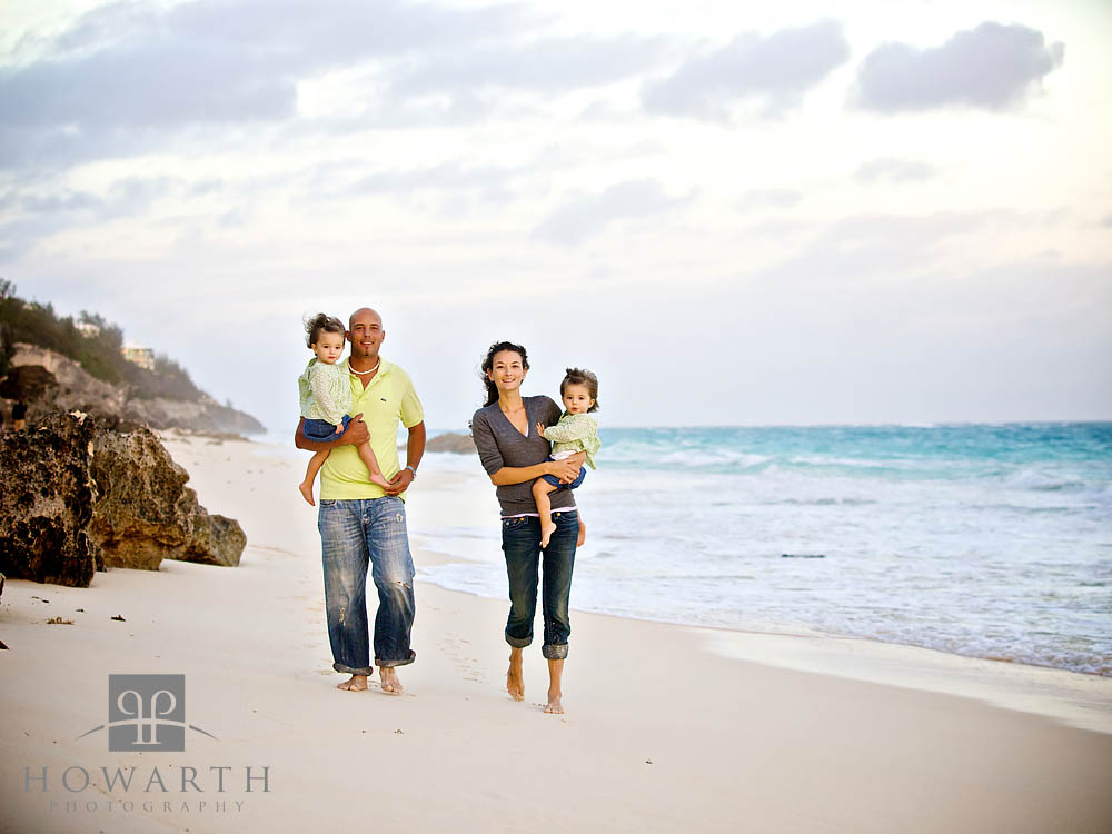 Mother and Father walking along the beach carrying their young twin daughters